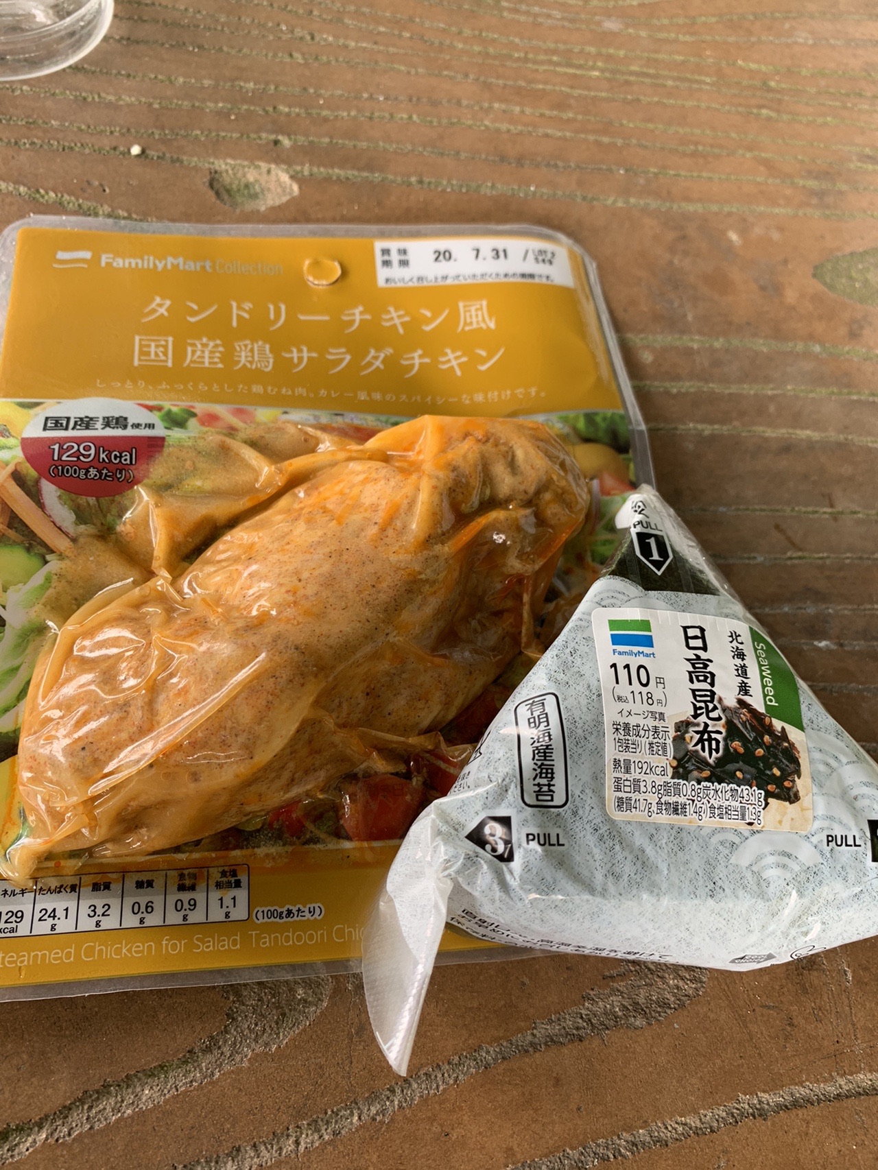 木のベンチの上に置かれた、コンビニのサラダチキンとおにぎり