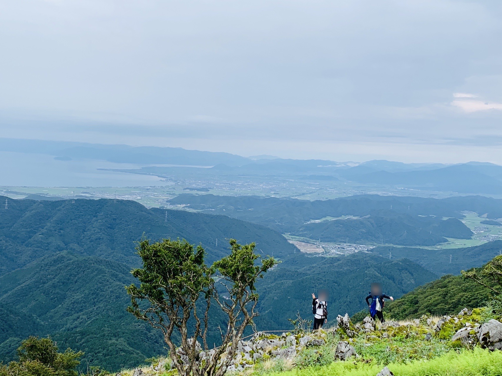 カルストの斜面に立つ2人と、その向こうに広がる山並みと琵琶湖。プライバシー保護のため顔にぼかしを入れています