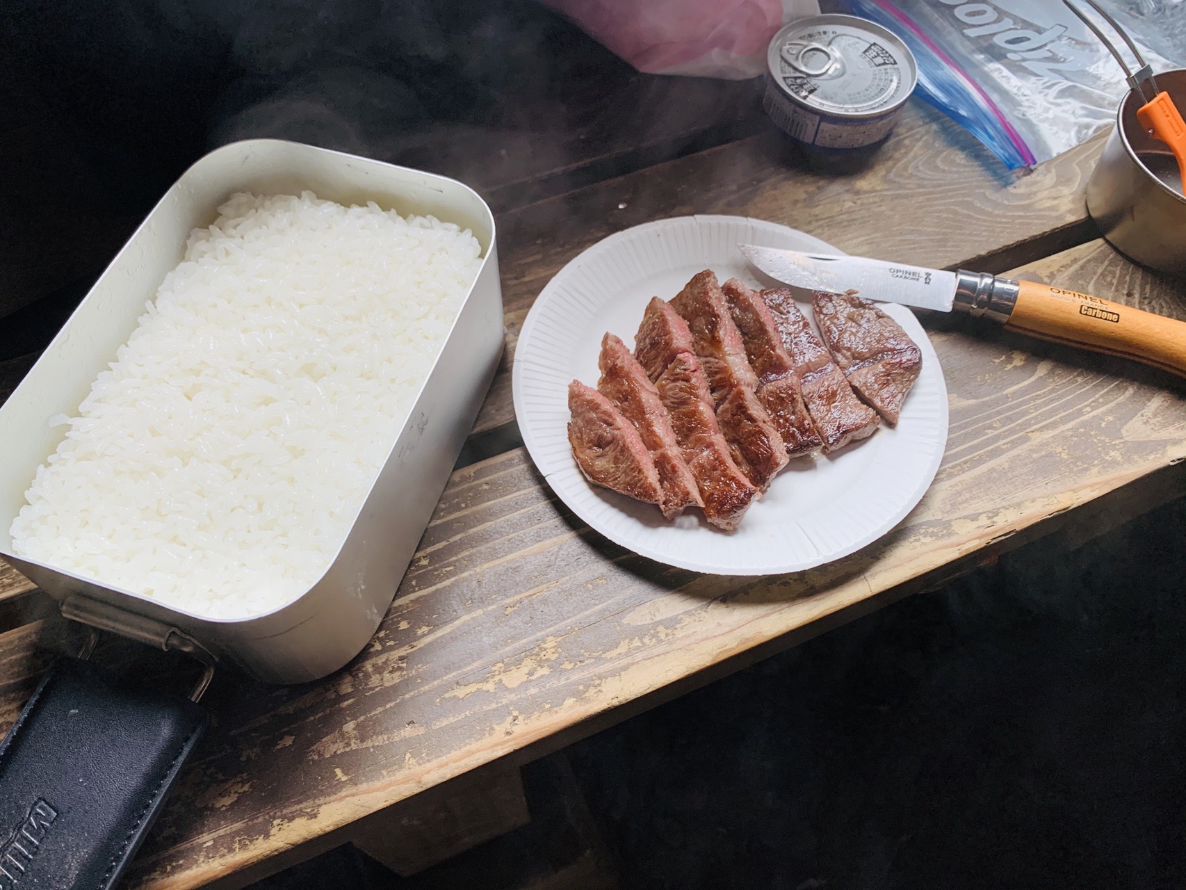 小屋の中のテーブルに並んだ、メスティンで炊いたご飯と、切り分けたステーキの皿