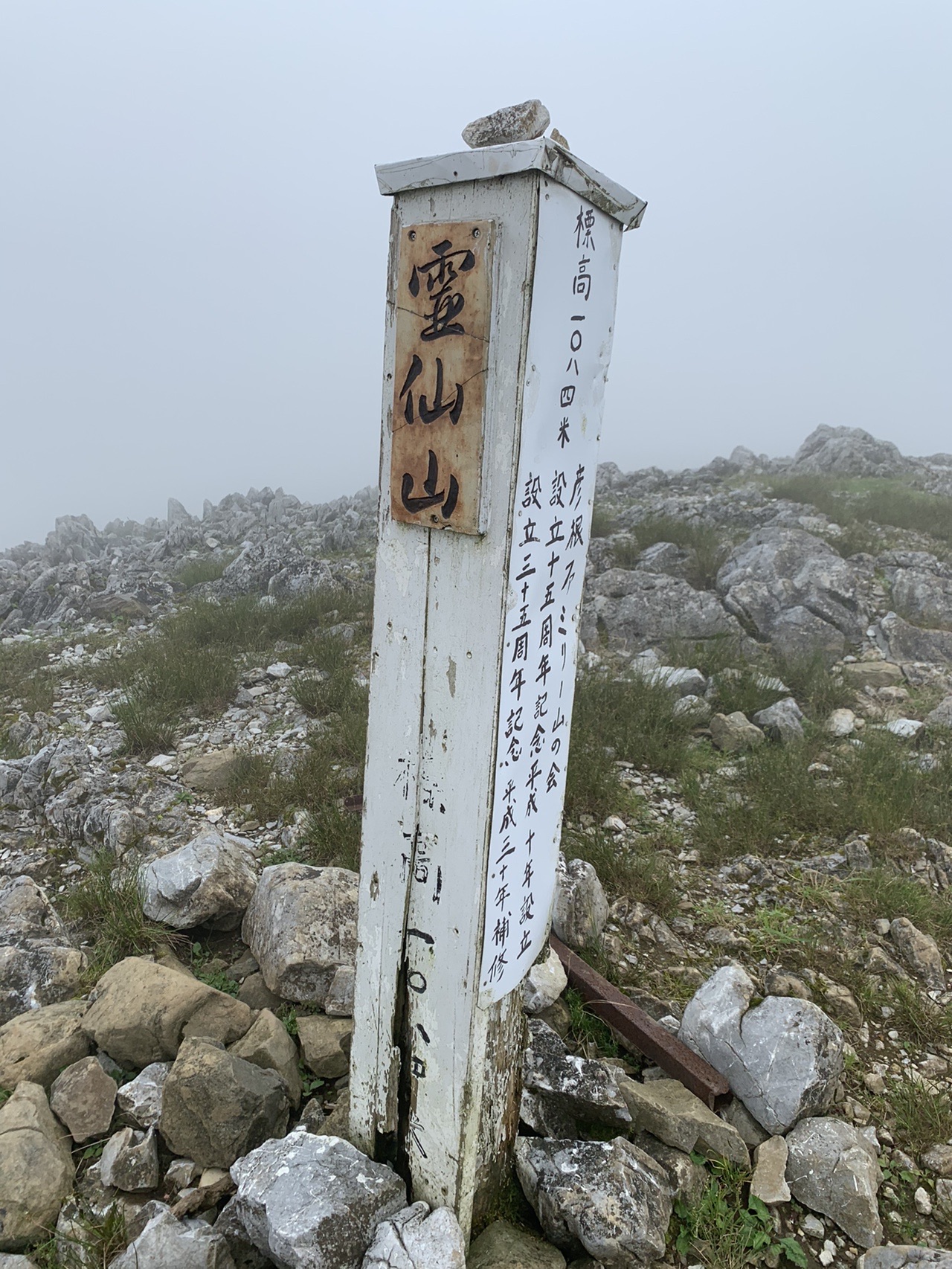 霧の中に立つ「霊仙山」の白い山頂標柱と、まわりの石灰岩