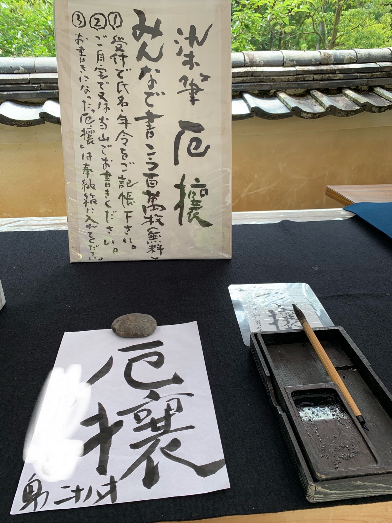 黒い台の上に置かれた半紙に、筆で「厄攘」と書かれている。硯と筆、案内の立て札