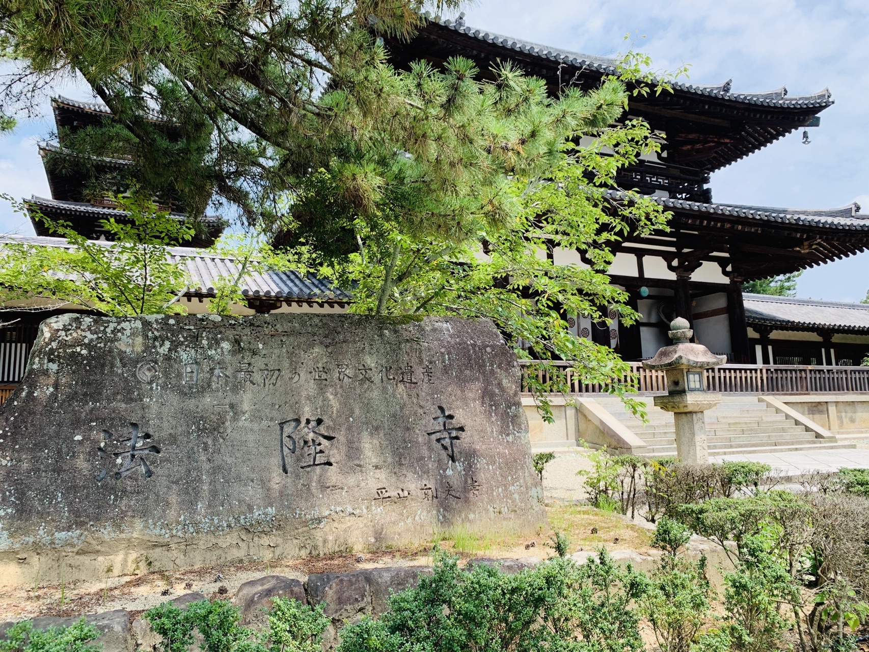 「法隆寺」と刻まれた石の寺号標と、その奥に見える五重塔と金堂の屋根