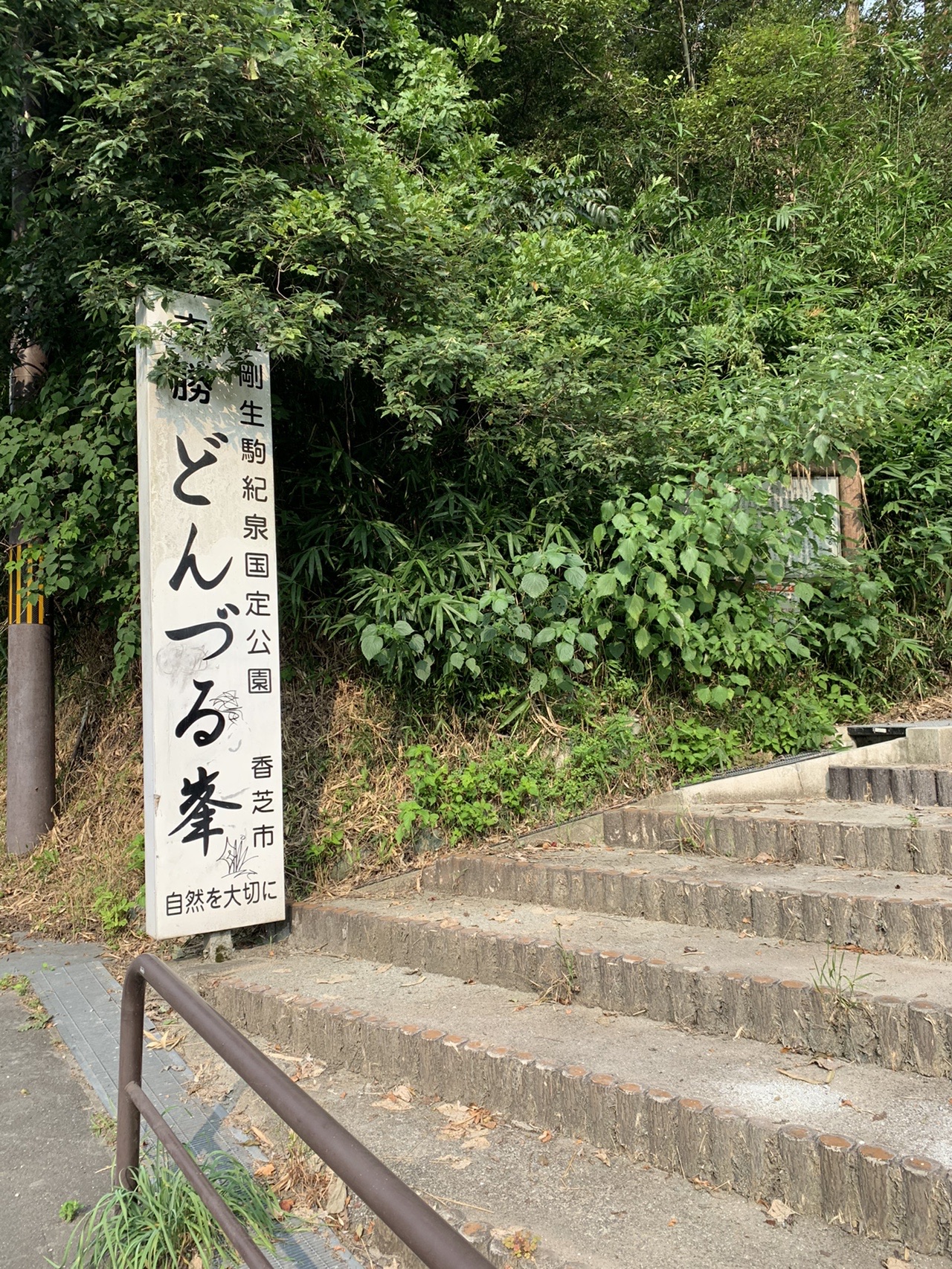 「どんづる峯」と刻まれた石柱と、その奥に続く階段。まわりは緑の木々