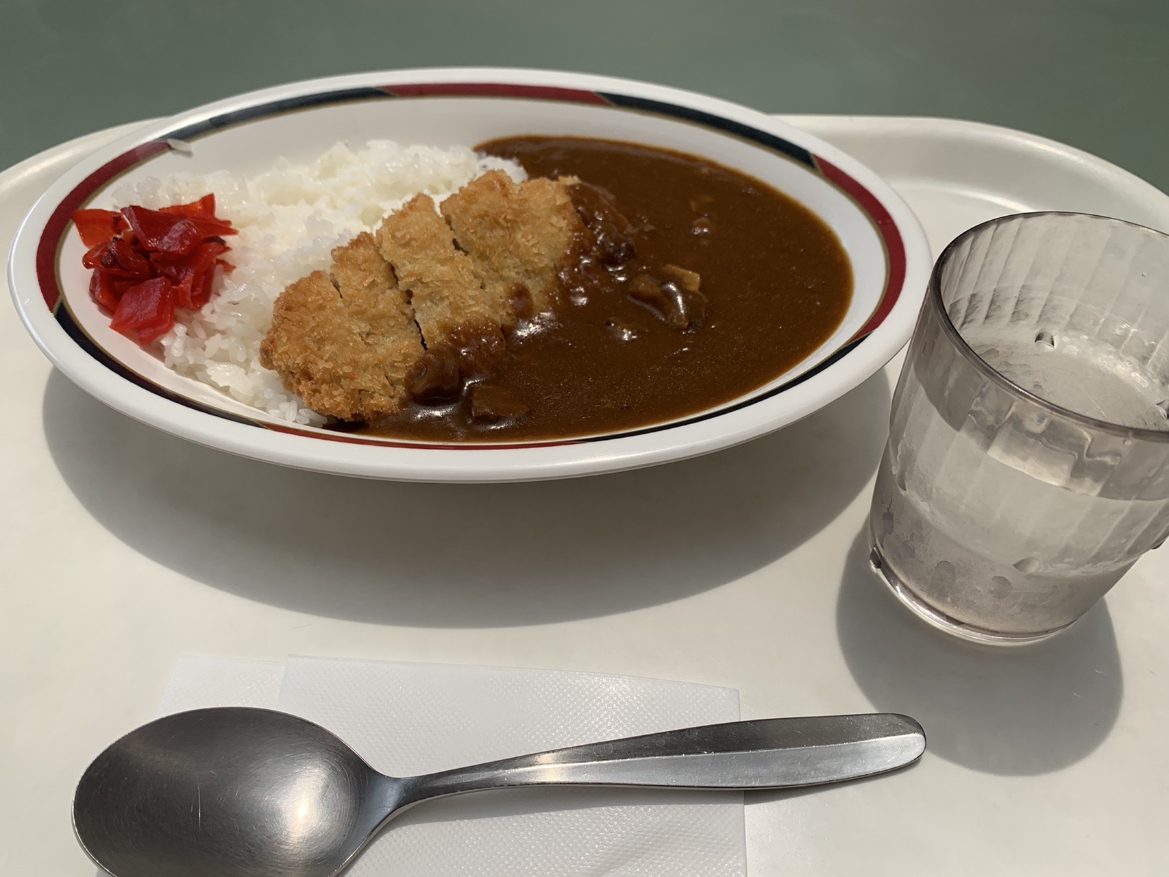 白いご飯の上にカツがのり、ルーがかかったカツカレーと、水のグラス、スプーン