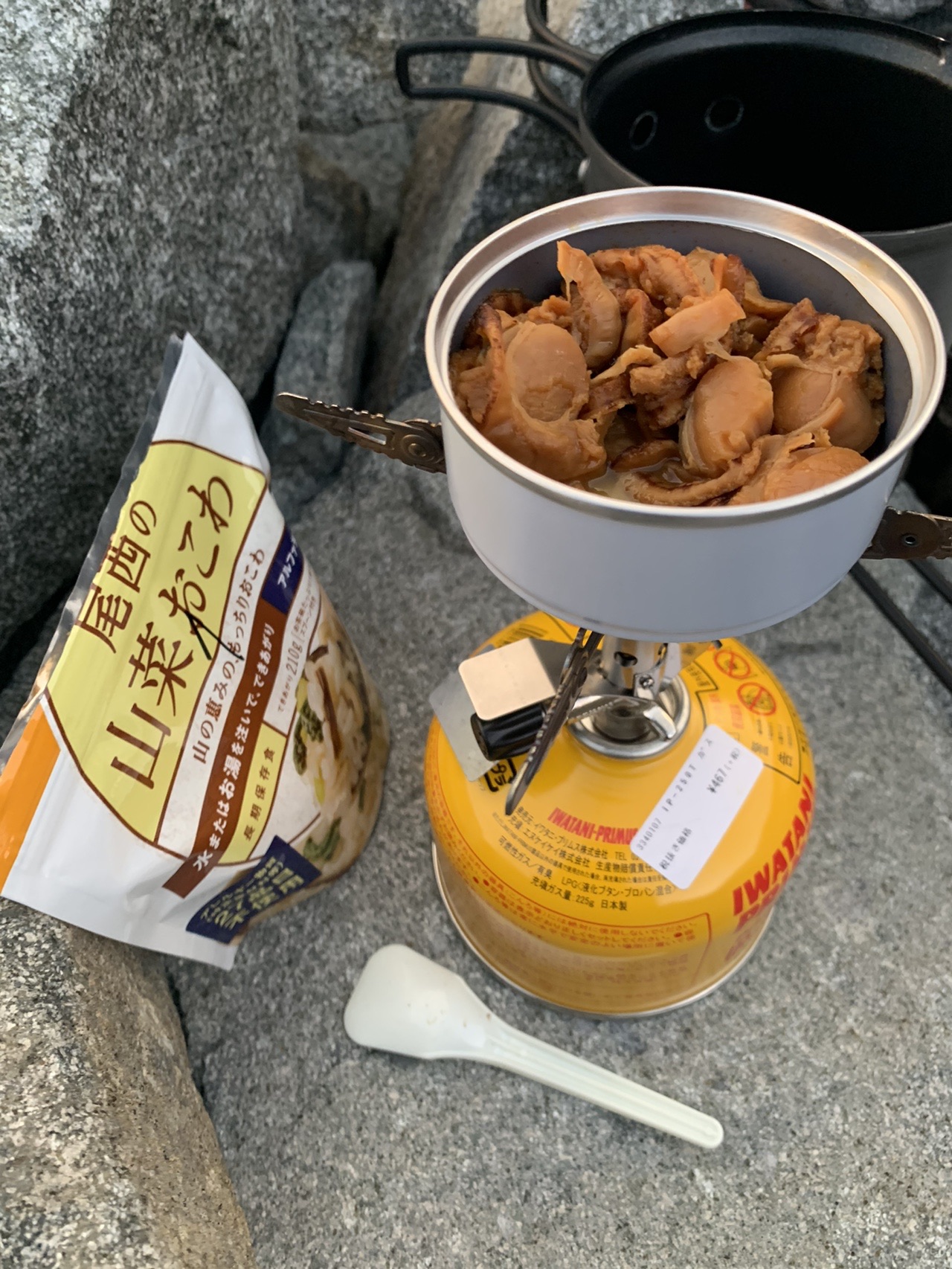 岩の上に置かれたコッヘルの中のホタテの缶詰と、アルファ米の袋