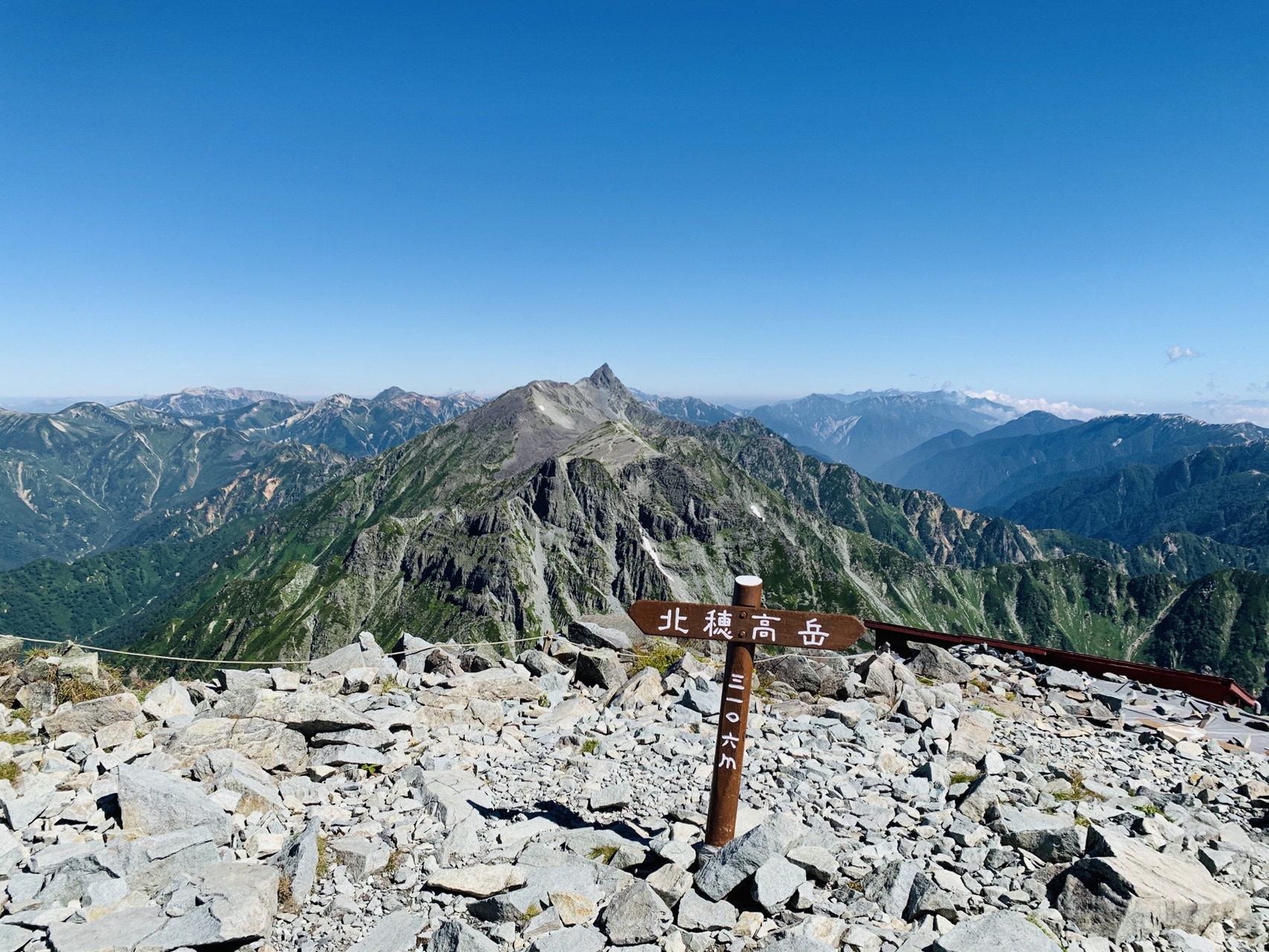 北穂高岳の山頂標識と、その向こうに尖った槍ヶ岳が見える稜線