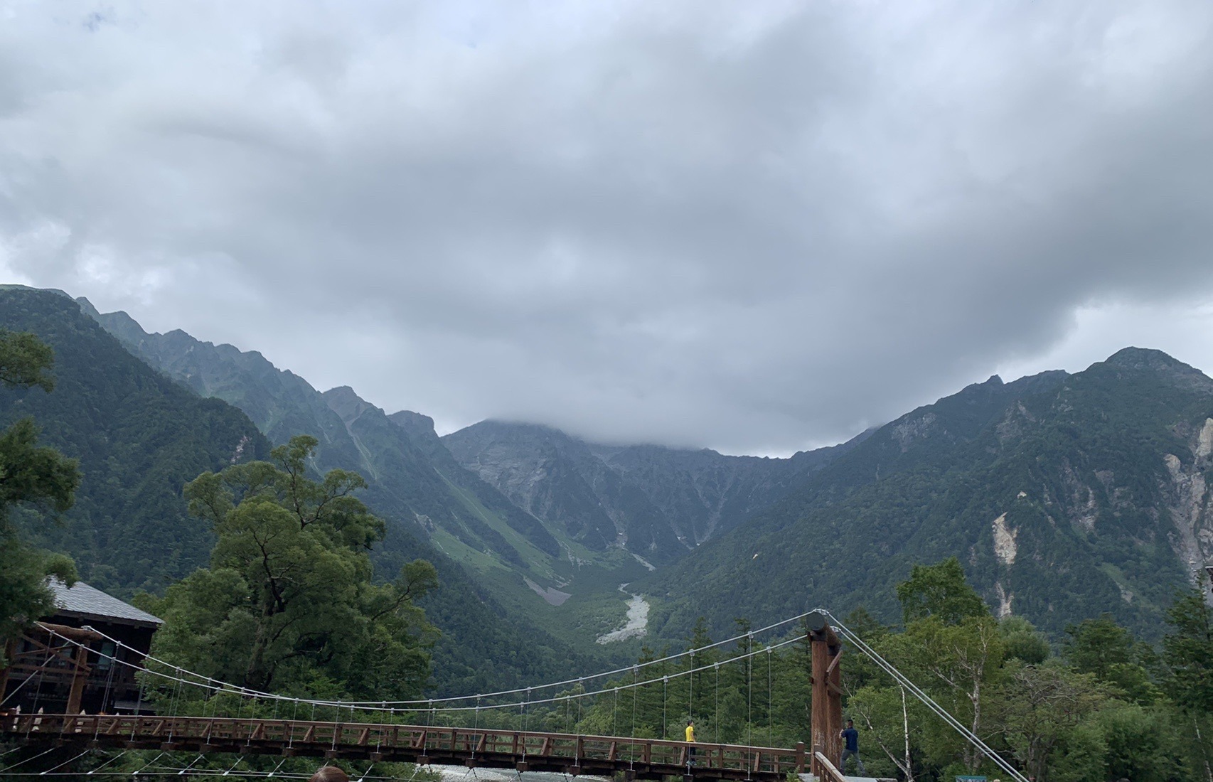 曇り空の下、河童橋の向こうに雲をかぶった穂高連峰が見える上高地の風景
