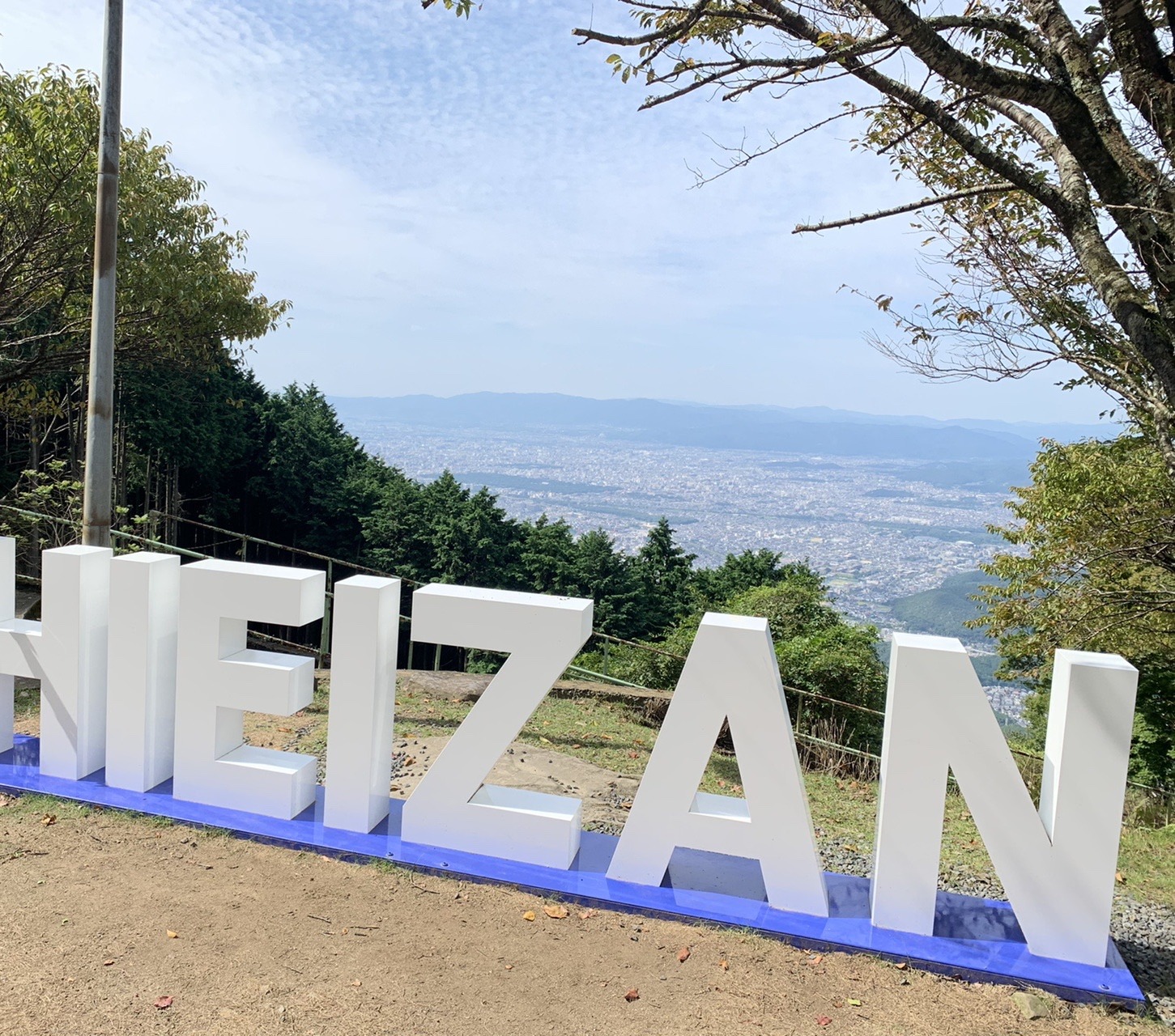 山の上に置かれた白い立体文字「HIEIZAN」と、その向こうに広がる京都市街
