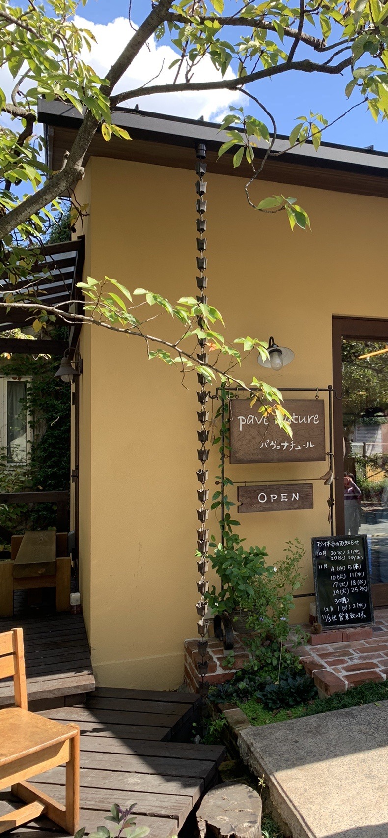 黄色い壁に木の看板がかかったパン屋の入口とテラス席