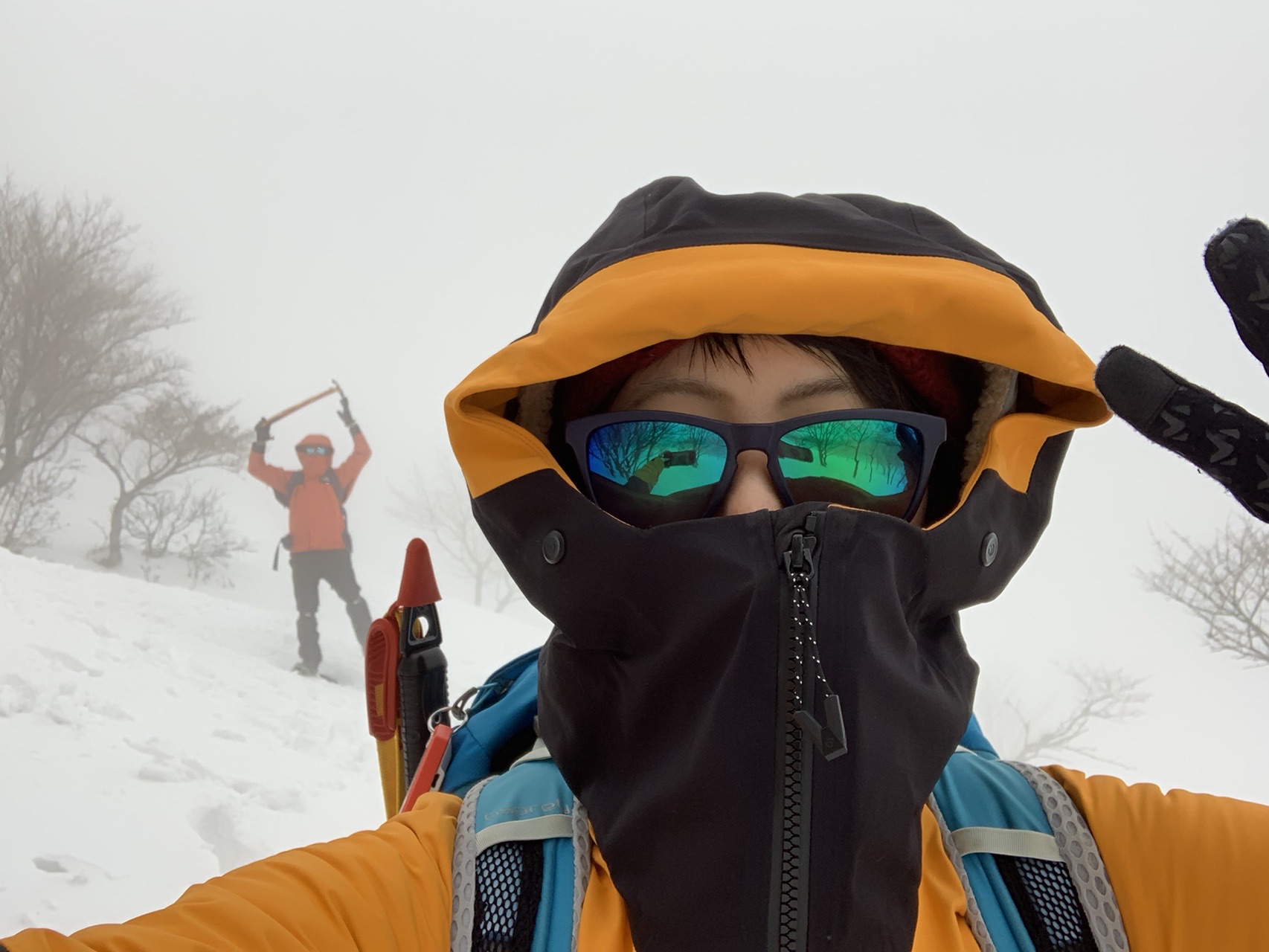 ゴーグルとバフで顔を覆った登山者の自撮り。背後は白い雪面