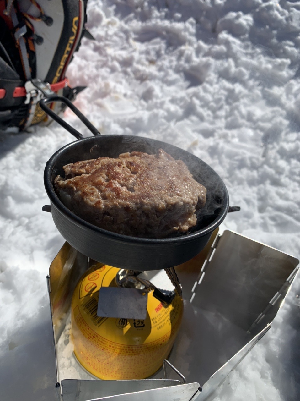 雪の上のバーナーとフライパンで焼かれたハンバーグ