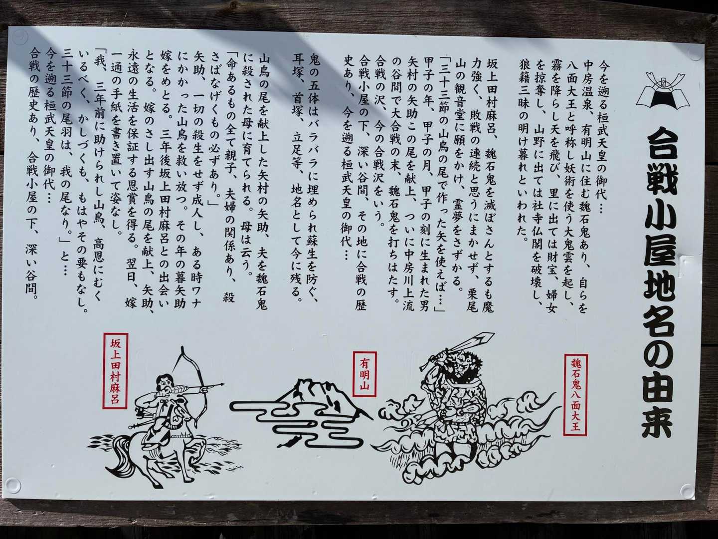 「合戦小屋地名の由来」と書かれた白い説明看板。坂上田村麻呂・有明山・魏石鬼八面大王の挿絵が描かれている