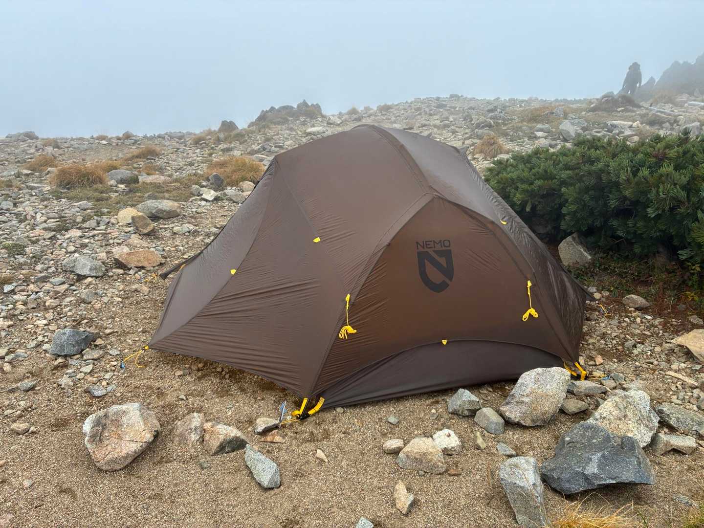砂利の上に設営された茶色のソロテント。背景はハイマツと岩