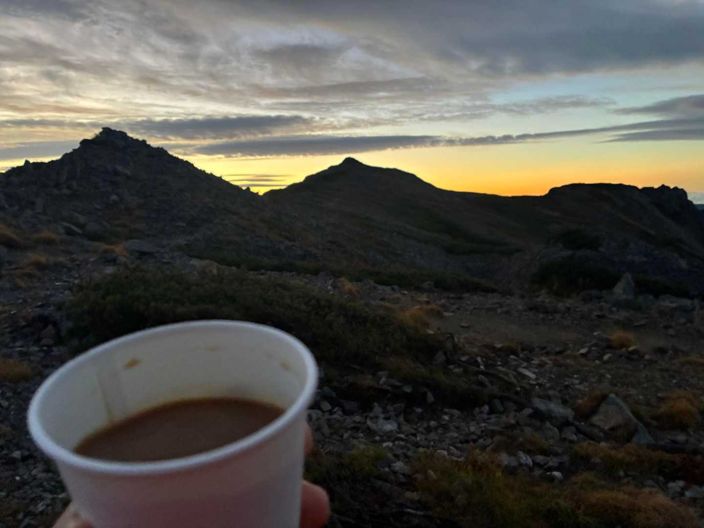 紙コップのコーヒー越しに見る夜明け前の稜線と、うっすら明るくなった空