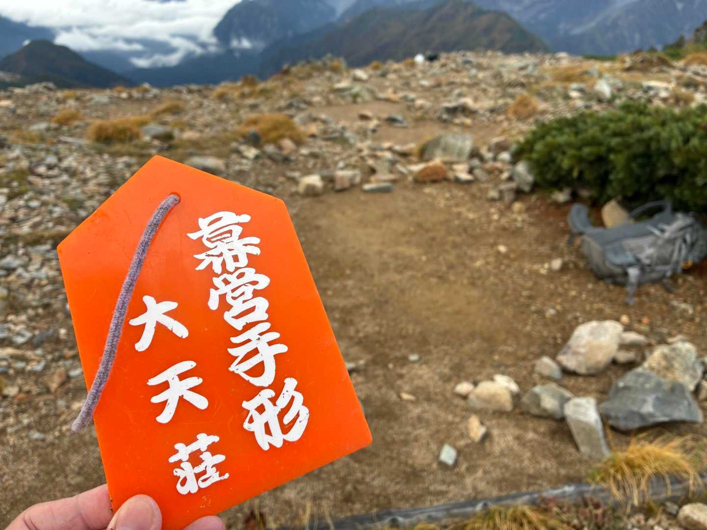 「幕営手形 大天荘」と書かれたオレンジ色の木札を手に持っている