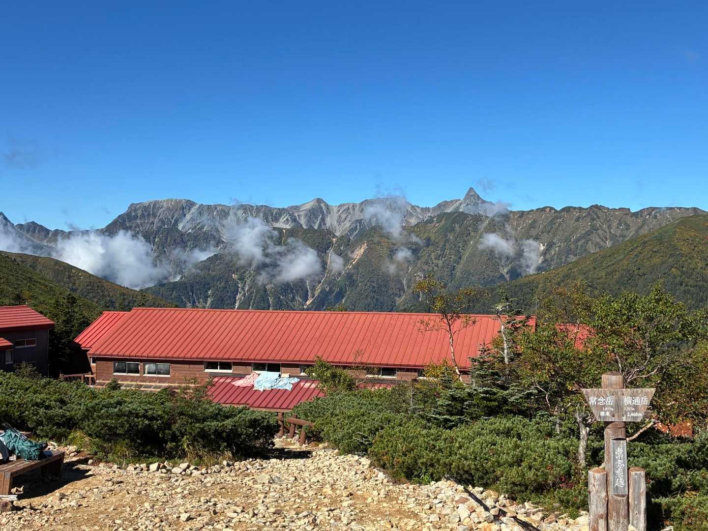 赤い屋根の常念小屋を見下ろす。背後に槍ヶ岳と穂高連峰の稜線が並ぶ