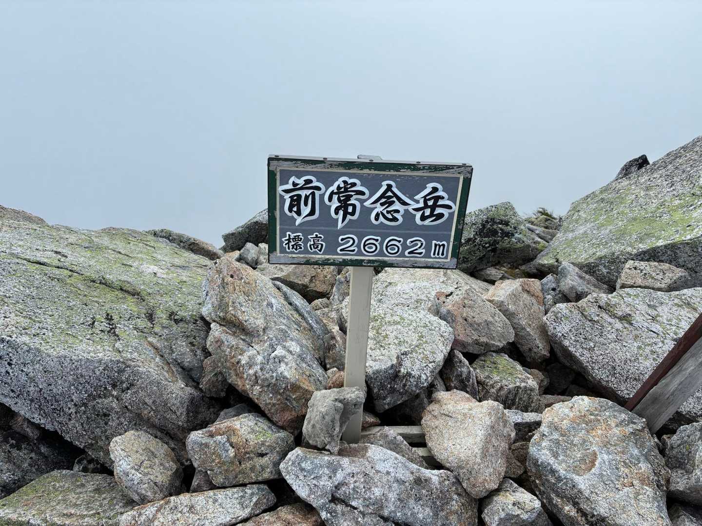 岩の積み重なった山頂に立つ「前常念岳 標高2662m」の黒い標識