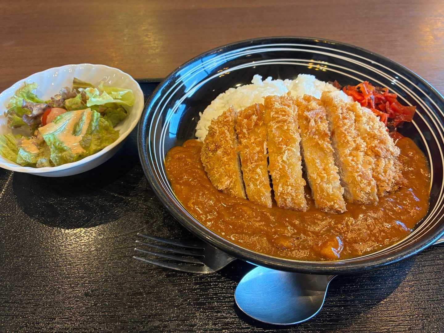 カツカレーとサラダの定食。皿に盛られたカレーの上に大きなカツが載っている